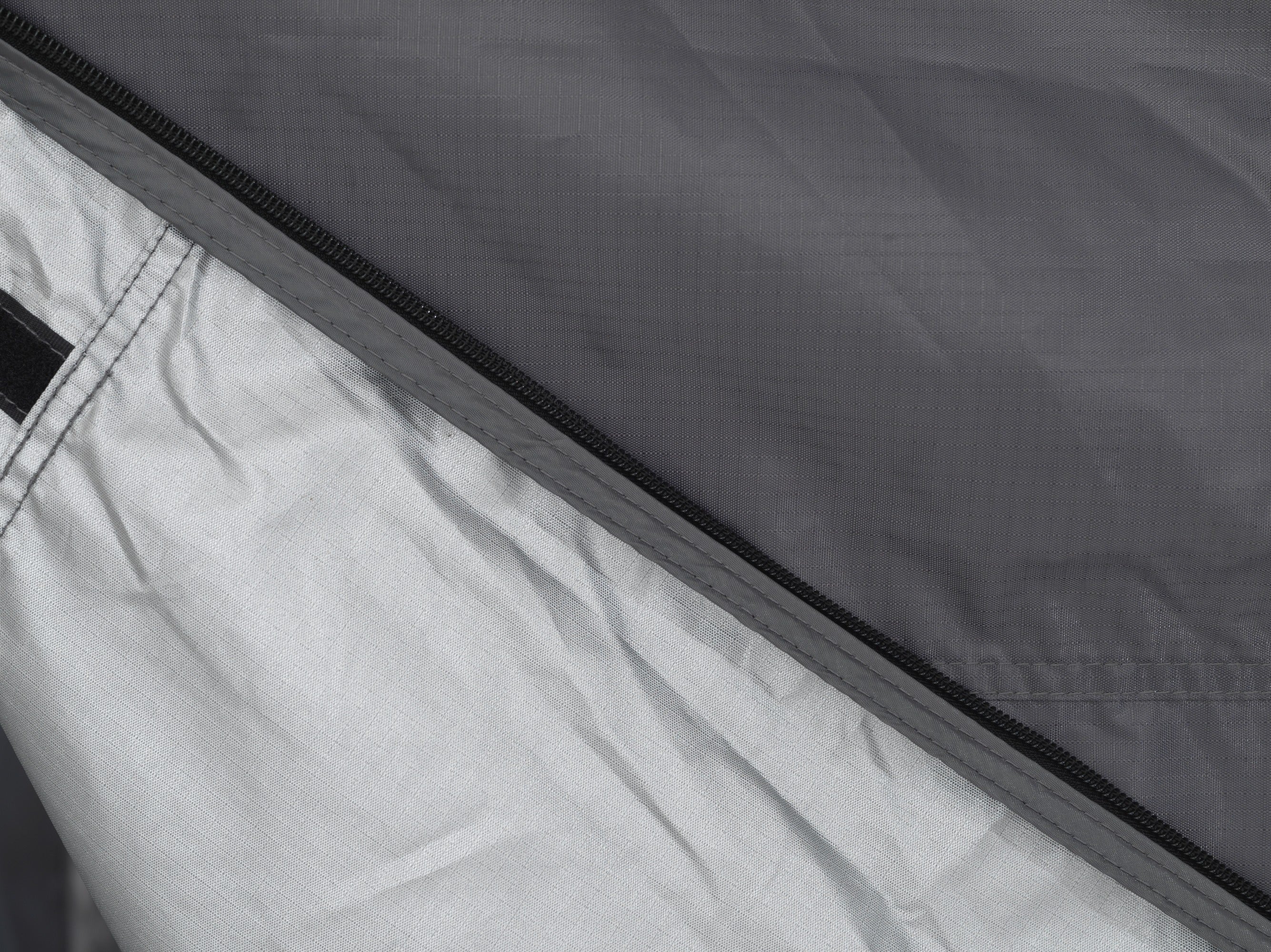 Close-up of a durable fabric with a partially unzipped black zipper, showing an inner silver-gray lining against a dark gray outer material.