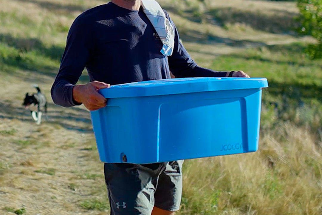 Person carrying the blue Nomad Sink across a grassy paddock, with a dog behind them